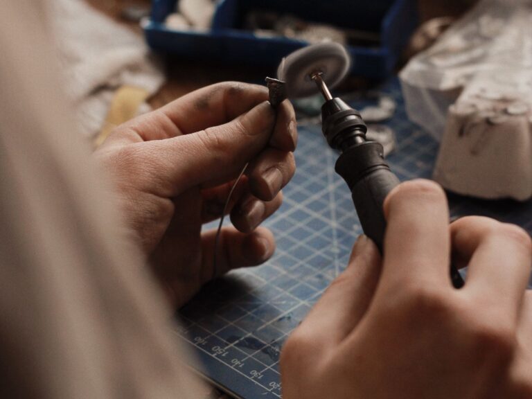 Hands polishing a silver jewelry piece with a rotary tool
