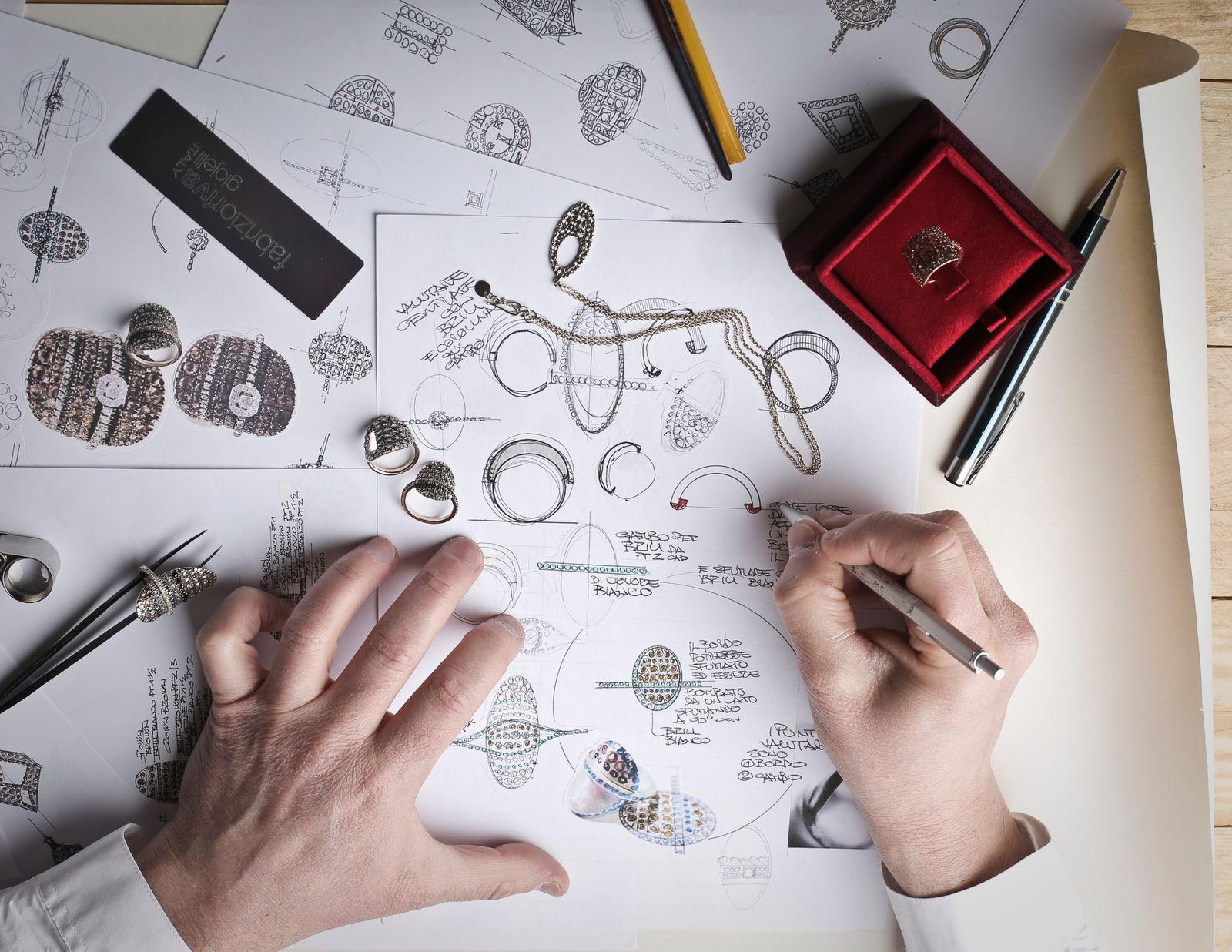 Jewelry workshop workbench with sketches, CAD ring design on a tablet and a craftsman setting a stone