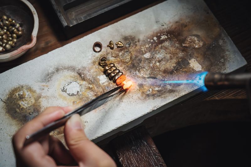 Jeweler using tweezers and a torch to finish a silver piece on the workbench