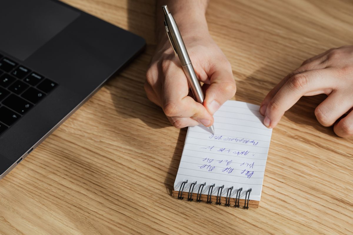 Buyer writing down jewelry specifications next to a laptop when preparing a wholesale inquiry